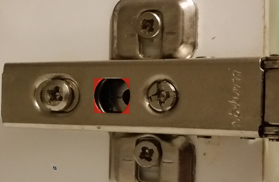 Close-up of a door hinge; red frame highlights a hole in the hinge plate.