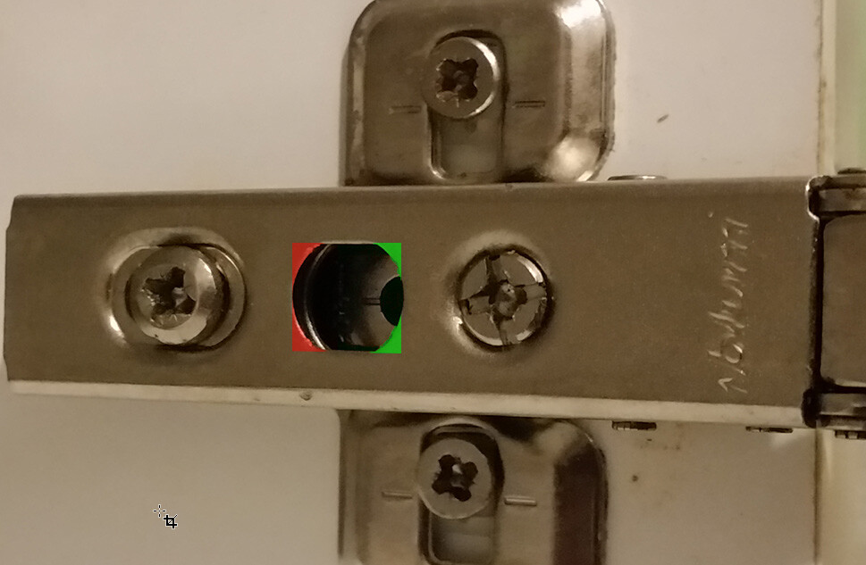 Close-up of a metal hinge with screws and a round hole in the center.
