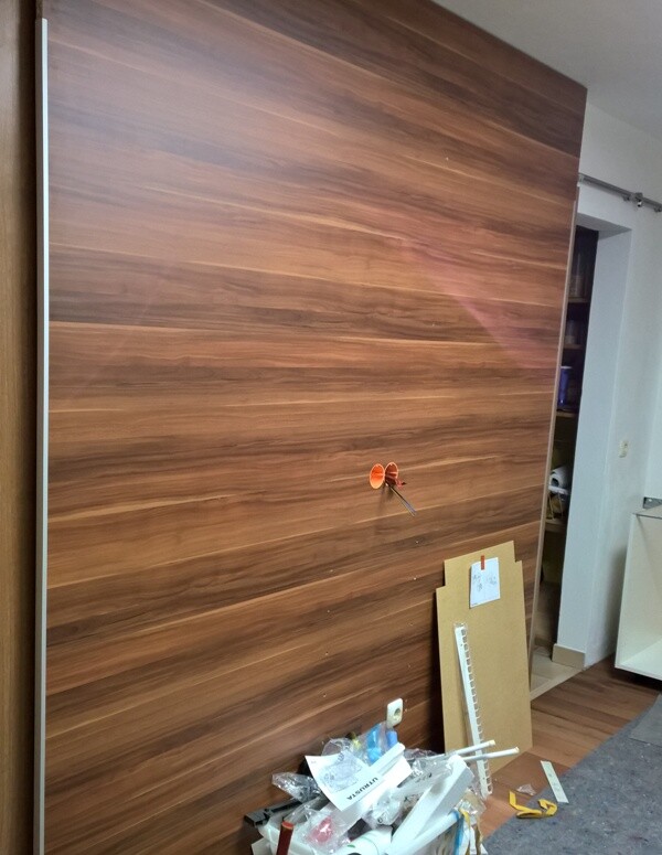 Large wooden cabinet door in a workshop, cardboard on the left, small orange component in the middle.