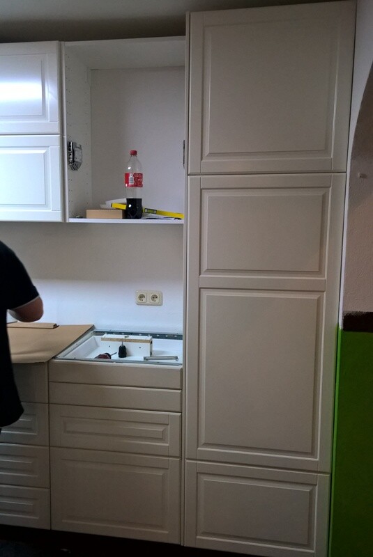 White kitchen units with cabinets, oven, and open niche; bottle and items visible.