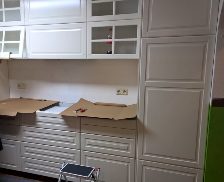 White kitchen fronts and wall cabinets, boxes on the countertop, small step ladder in front.