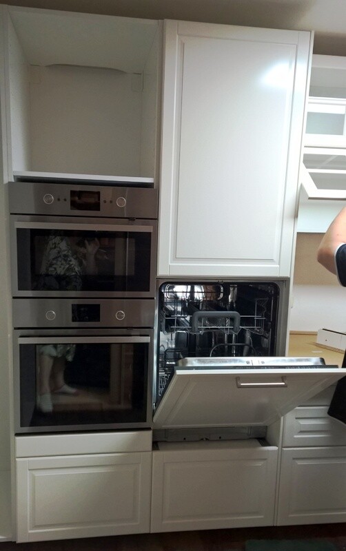 Modern kitchen with white cabinets; dishwasher open, built-in ovens next to it.