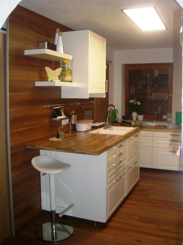 Modern kitchen with wooden wall, white island, bar stools, sink, and window with flower box.