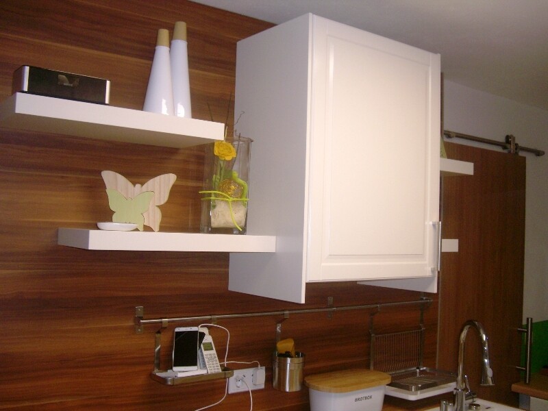 White wall cabinets and shelves against wood-colored kitchen wall; butterfly decoration, yellow vase, sink.
