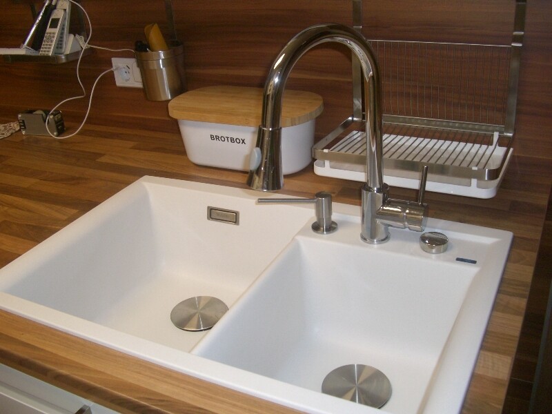 Double-bowl sink with modern stainless steel faucet, bread box, and drying rack on wooden table.