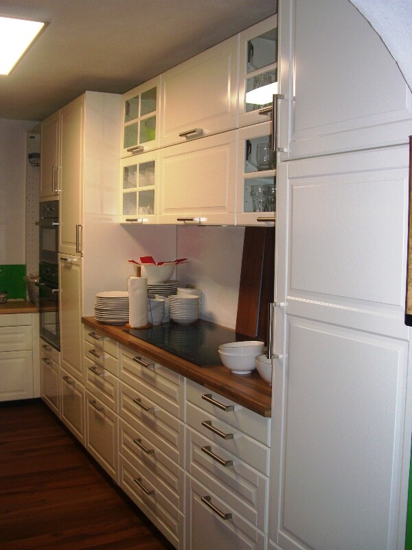 White kitchen unit with glass fronts, dishes on the countertop, and oven on the left.