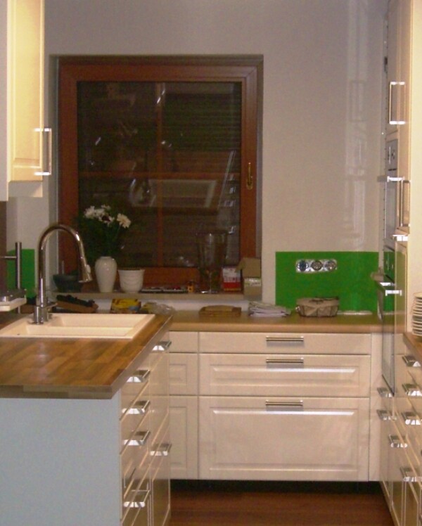 Kitchen with white cabinets, wooden countertop, sink, window, and green backsplash.