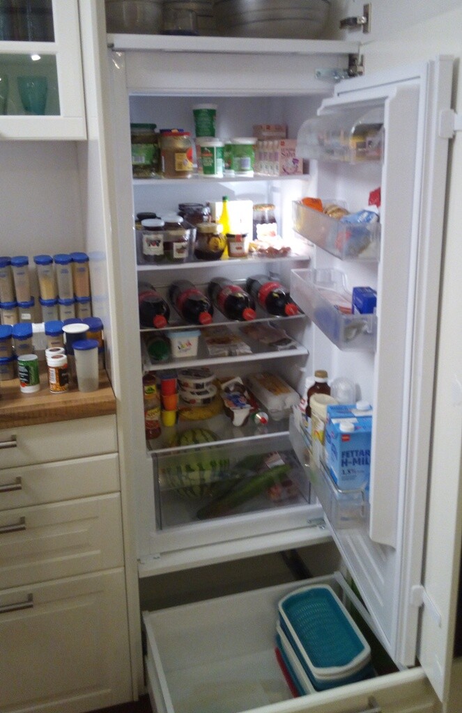 Open refrigerator full of jars, bottles, and food, fruit in the lower compartment.