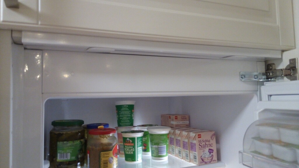 Open refrigerator with jars, yogurt cups, and dairy products on the inner shelf.