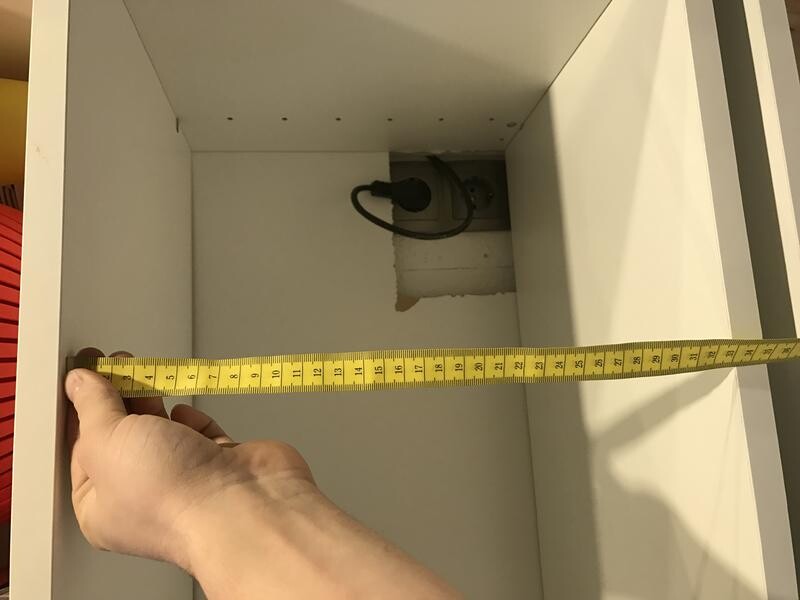 Hand misst Breite eines weißen Küchenschranks mit Maßband