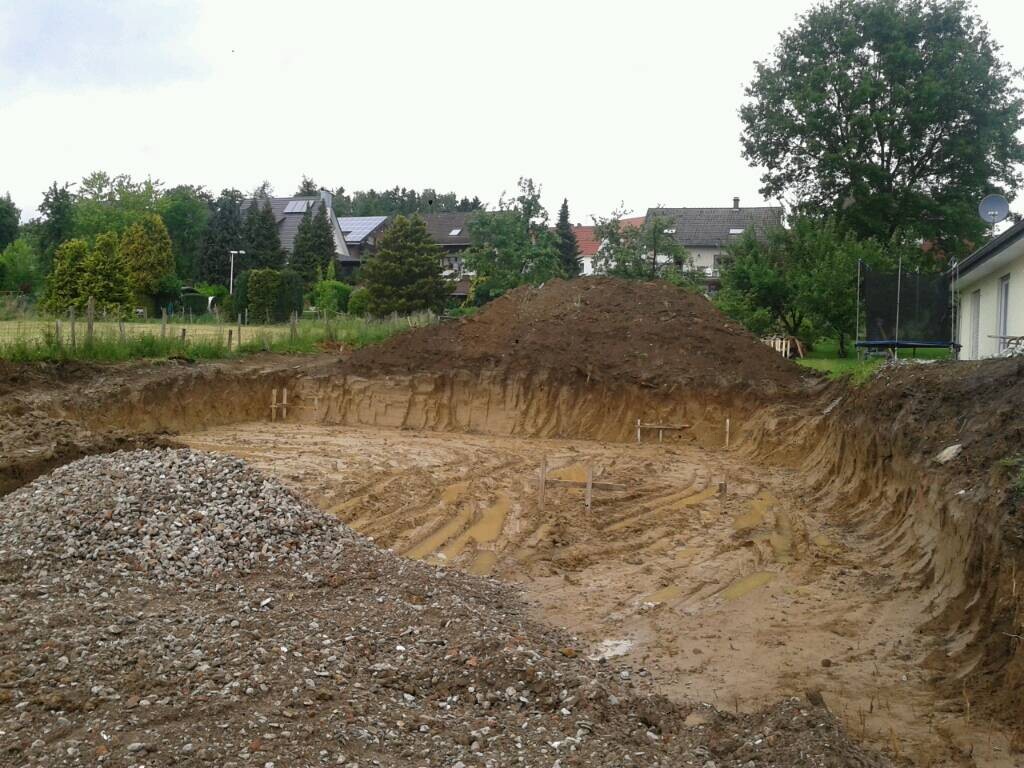 Große Baugrube mit Erdaushub und Kieshaufen in Wohngebiet, Häuser im Hintergrund