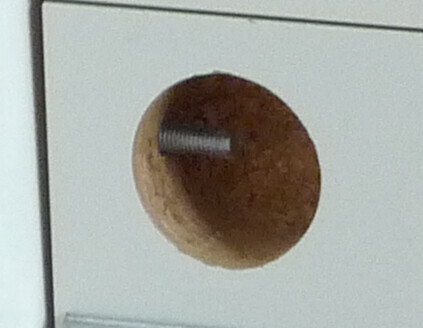 Close-up of a round drill hole in light-colored furniture panels with a bolt.