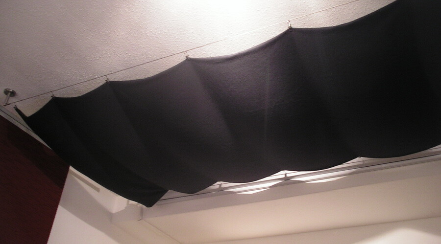 Black fabric covering hangs from the ceiling as a ceiling cladding in an interior space.