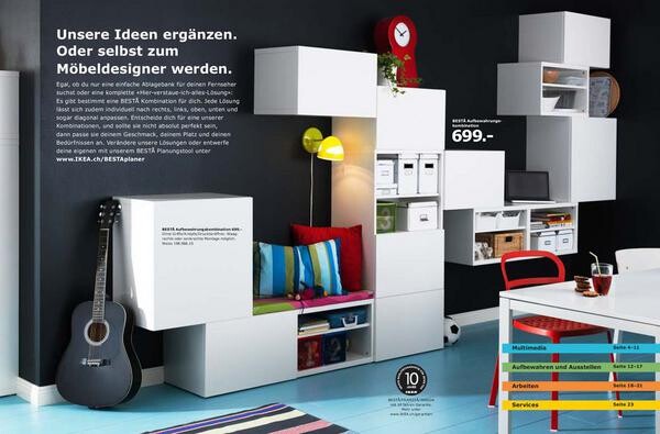 Modular white living wall made of shelving cubes with a guitar, colorful cushions, and a desk.