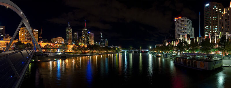 Nighttime photo of a city by a river with illuminated skyscrapers and a bridge.