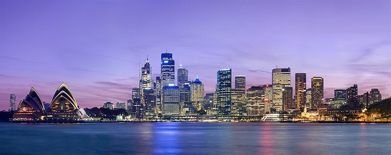 Night view of the Sydney skyline with the Opera House on the left and illuminated skyscrapers at the harbor.