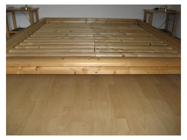 Low wooden bed frame with slatted base on light wooden floor in the bedroom