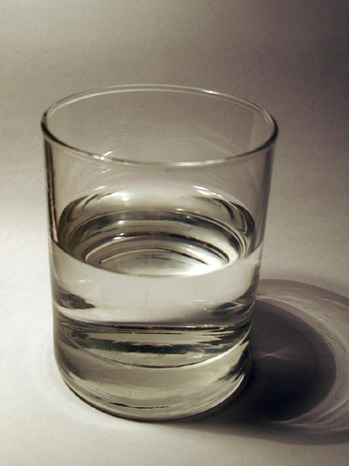 Clear glass of water on light surface with shadow