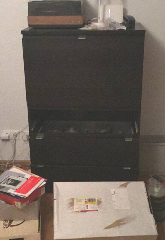 Dark cabinet with shelves, papers, and boxes in a messy room