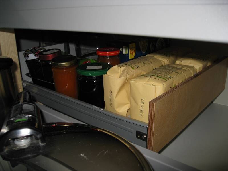 Opened kitchen drawer with jam jars, cans, and storage packaging.