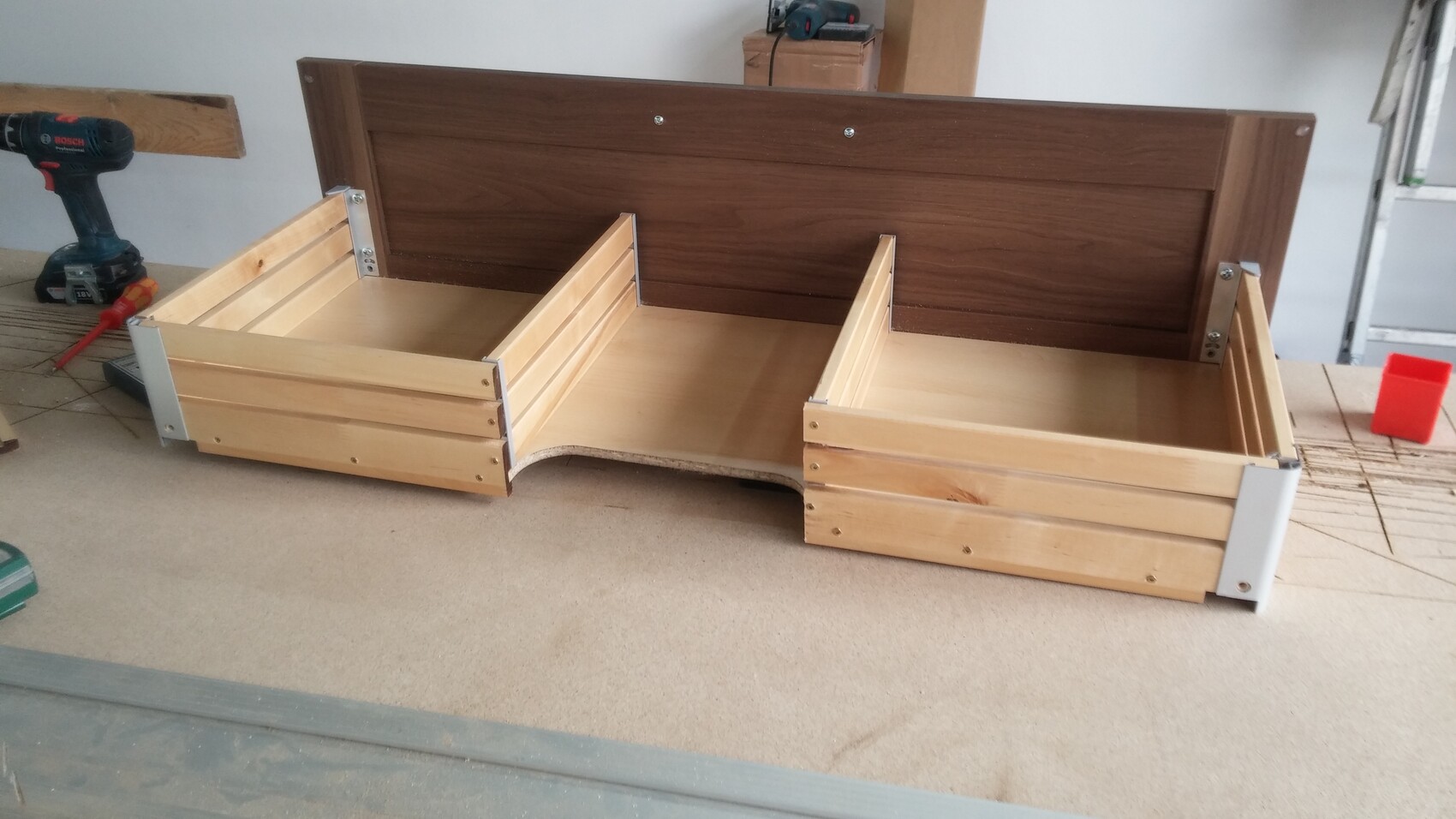 Wooden bed frame with dark headboard and two side storage boxes in a workshop