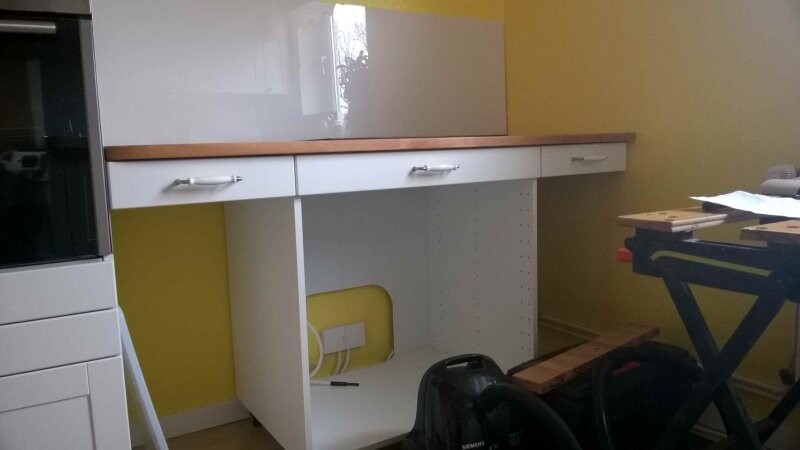 Kitchen with yellow wall, white base cabinets, open shelf and vacuum cleaner.