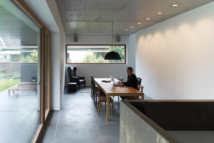 Modern open living area with dining table, laptop, cozy seating area, and view of the garden.