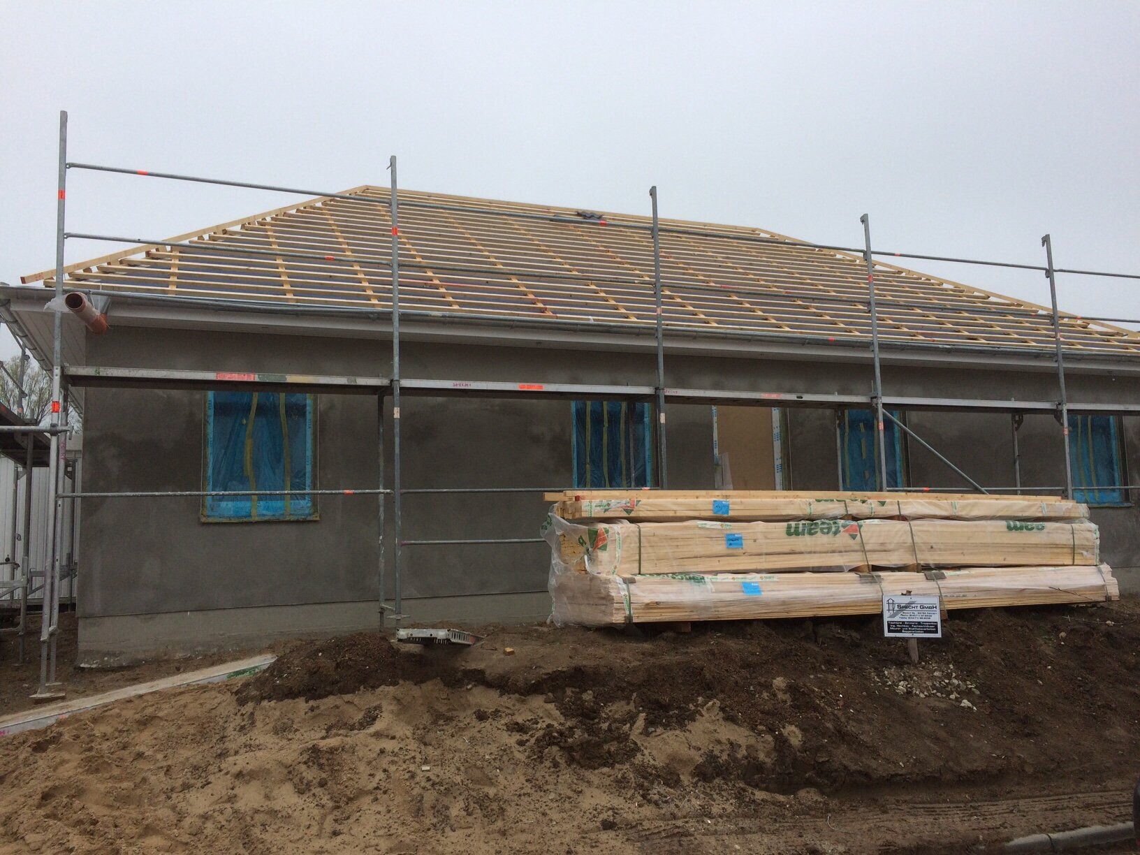 Wooden roof structure on the shell of a single-family house with scaffolding and construction timber in the foreground