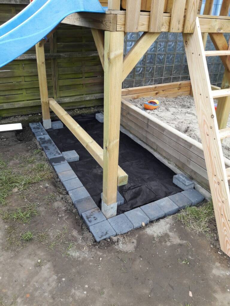 Substructure of a wooden playset with wooden frame, foundation blocks, and paving in the garden