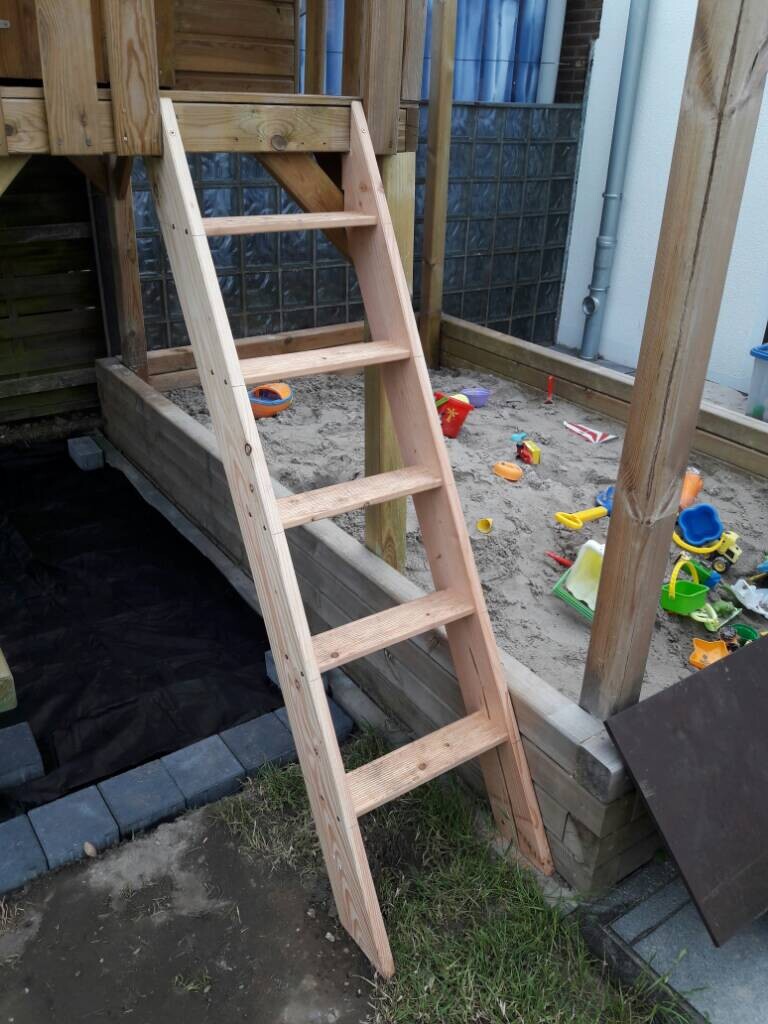 Wooden ladder as stairs to a play tower in the garden with toys around