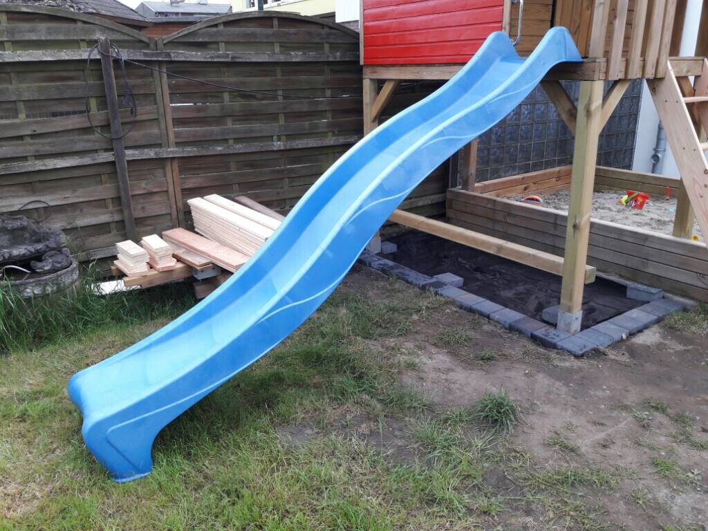 Blue slide on a wooden playset in the garden with sandbox