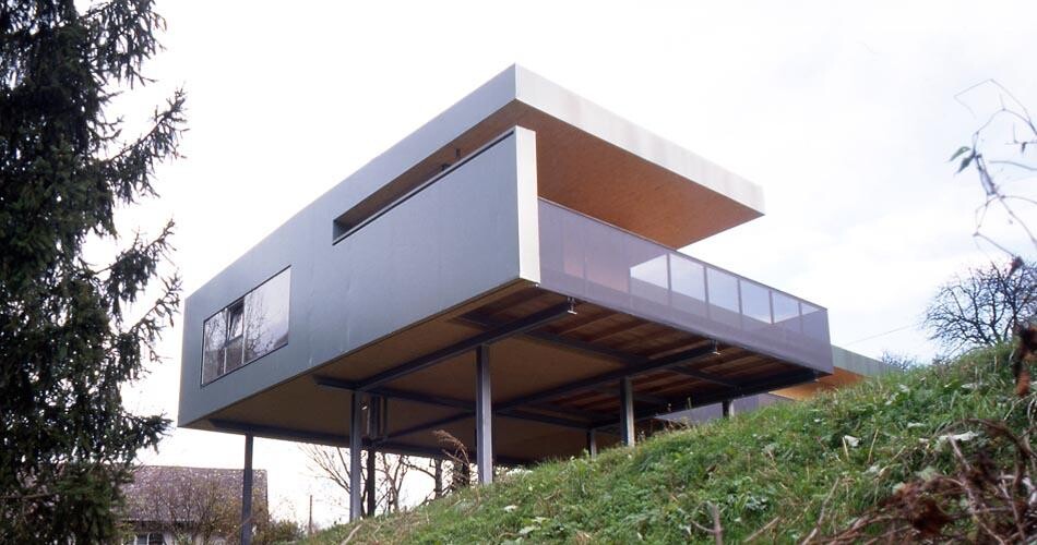 Modern house on stilts over a slope; rectangular design with glass balcony