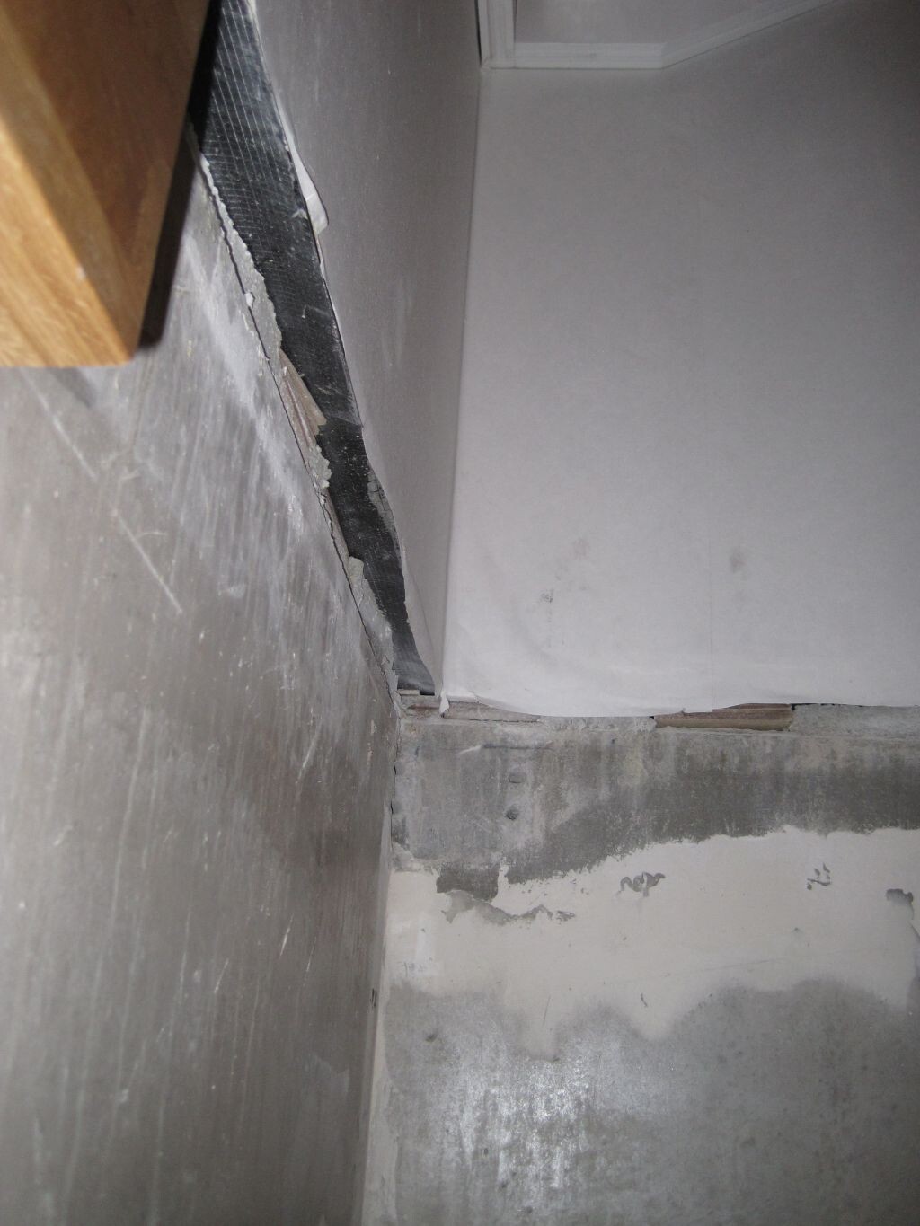 Basement corner with damaged wall, flaking plaster and moisture on the concrete floor.