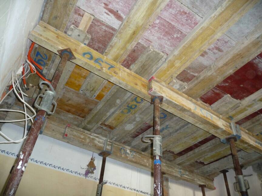 Unterbau einer Decke: Holzträger, Stützen und lose Kabel.
