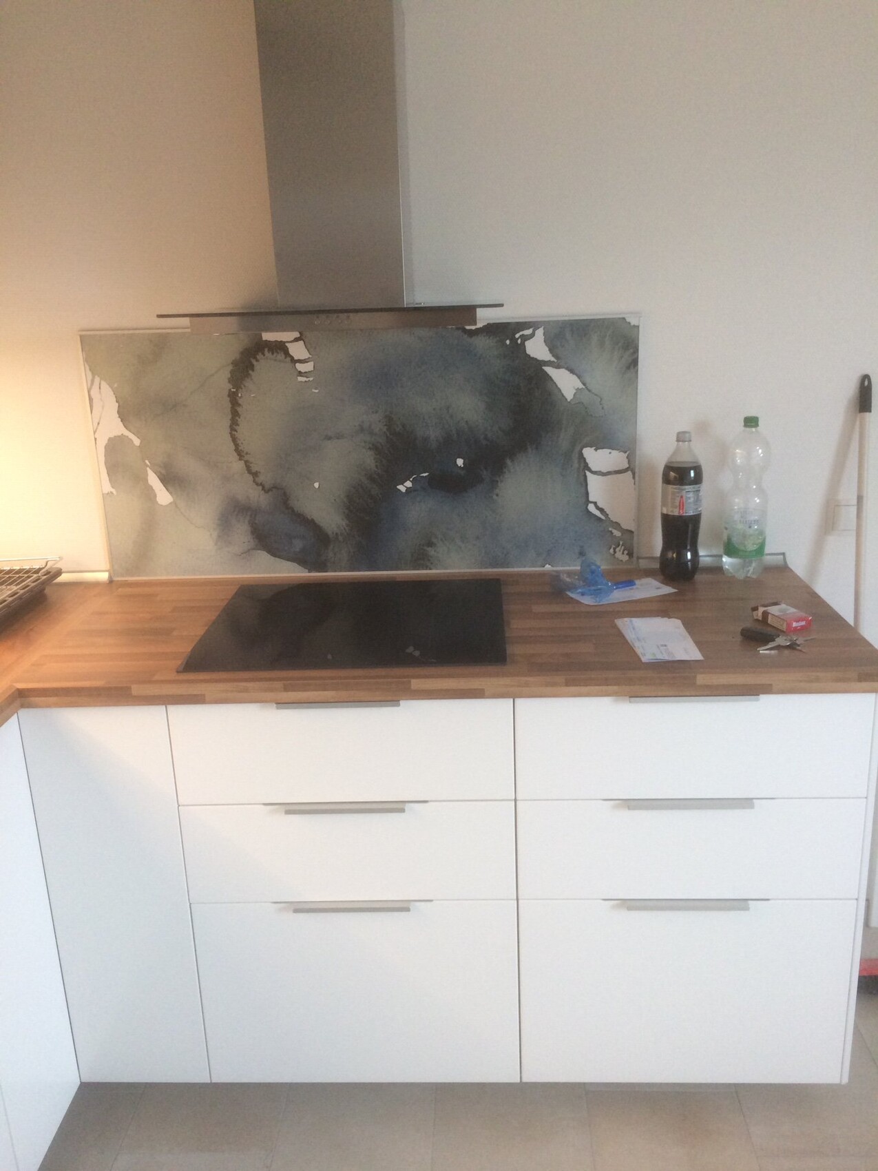 Modern kitchen: induction cooktop, white cabinets, wooden countertop; abstract blue-tone artwork behind the stove.
