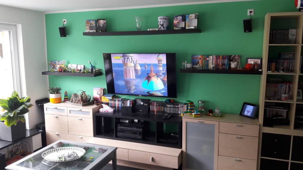 Living room with green accent wall, TV, shelves, plants, coffee table