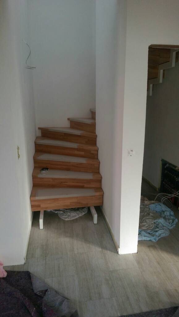 Wooden staircase indoors, construction phase, white walls, clothing on the floor.