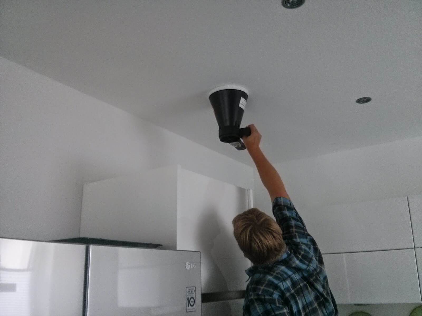 Man installing ceiling lamp in modern kitchen, refrigerator visible