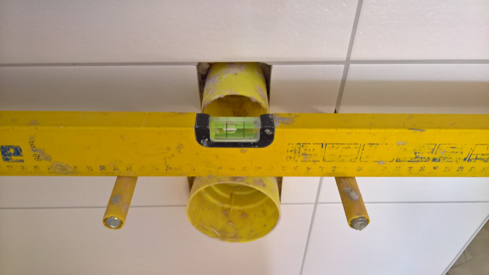 Yellow pipe passing through tiled wall with spirit level during interior installation