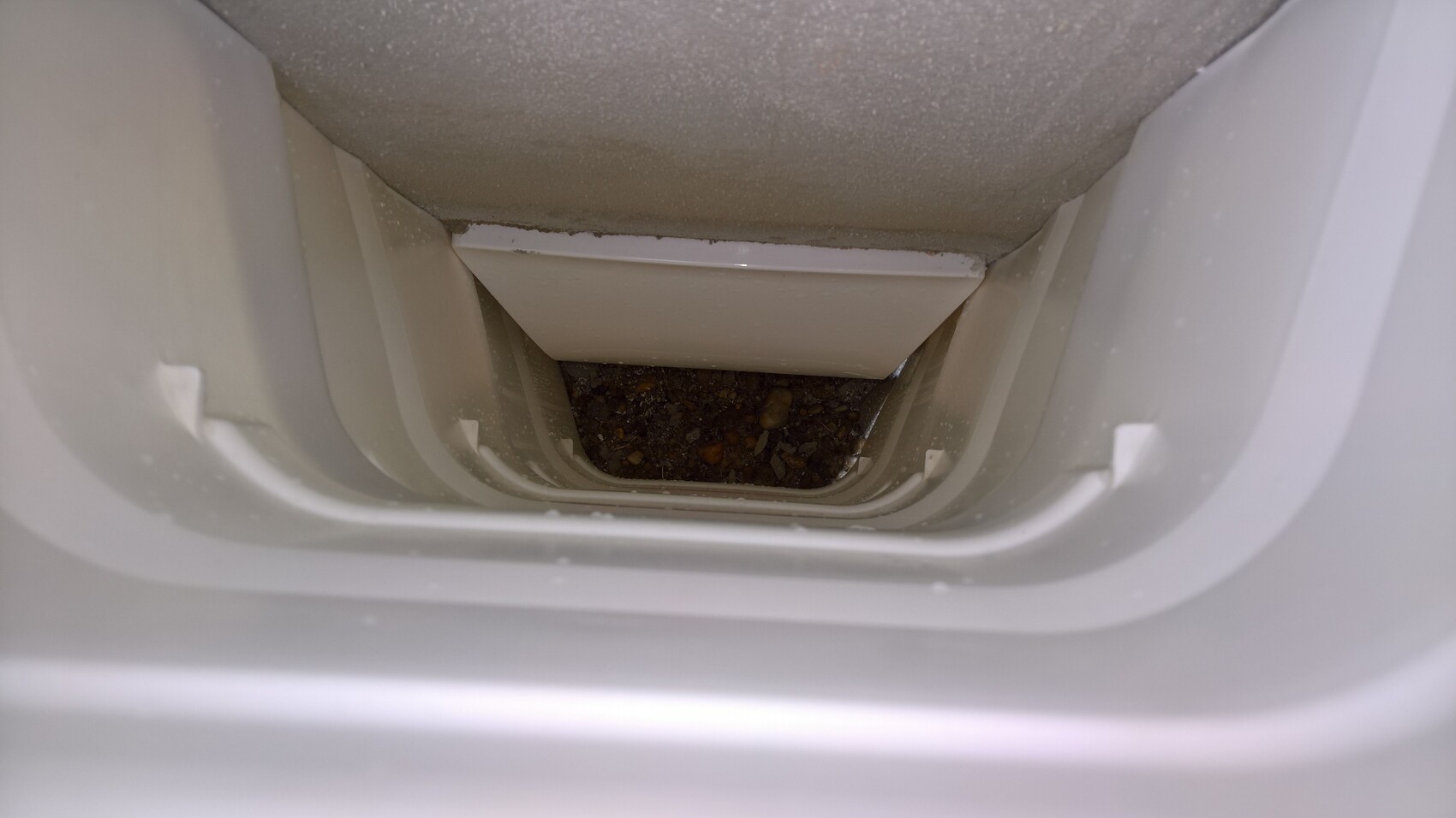 Interior view of a narrow drainage shaft with stones at the bottom, with white plastic walls.