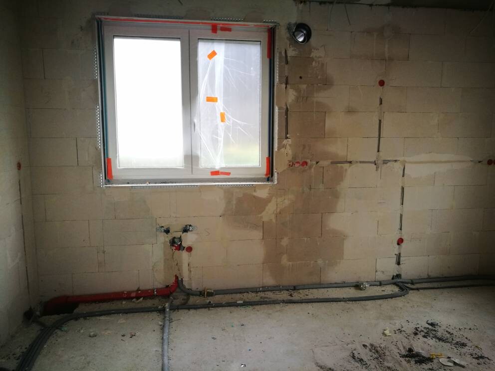 Construction site interior with window, unplastered walls, and visible water pipes.