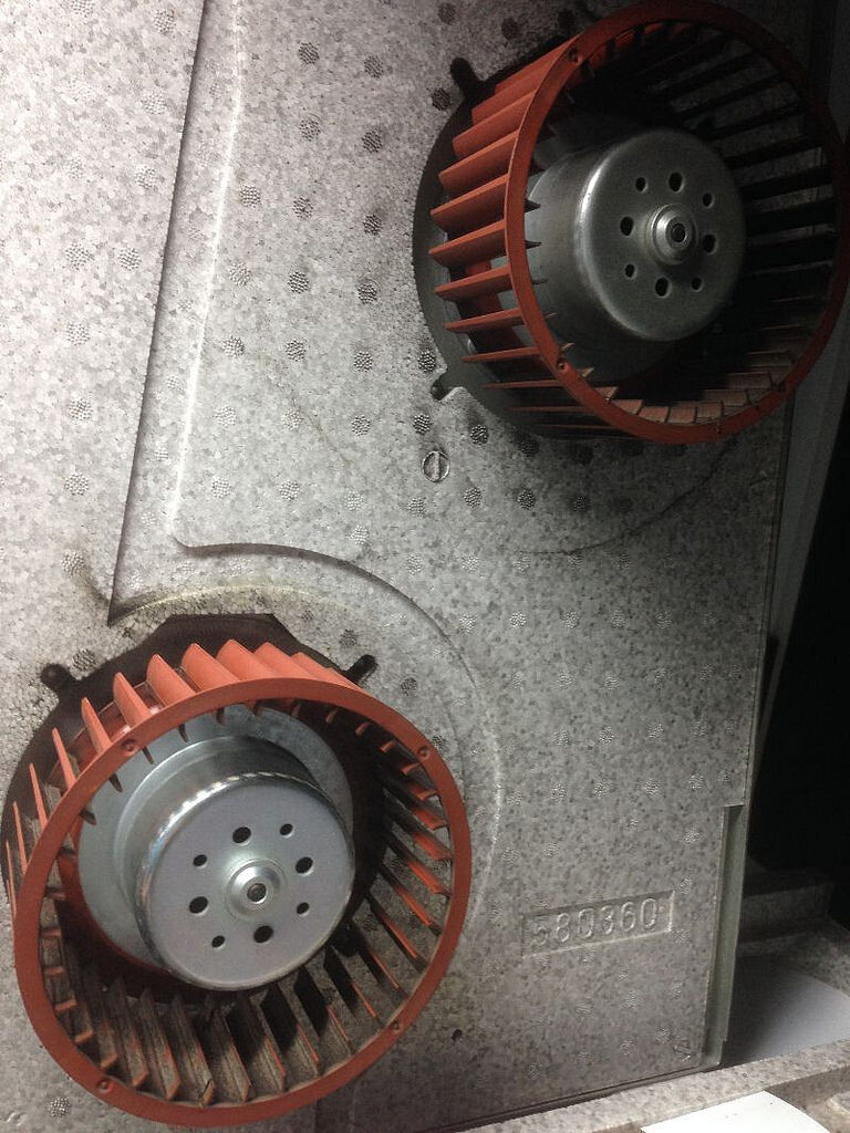 Two red fan wheels in a gray metal housing, part of a ventilation system.