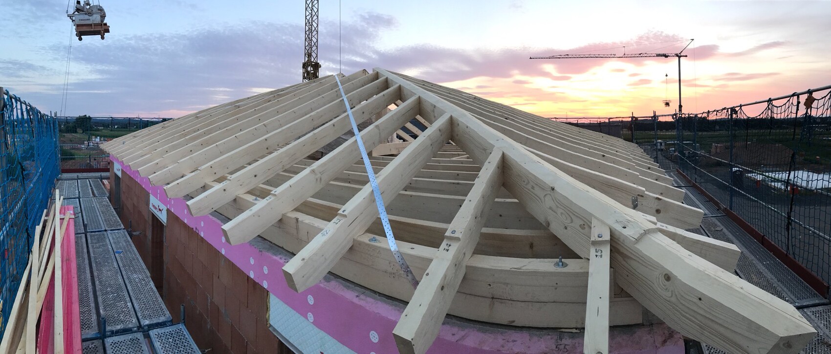 Wooden roof structure at the construction site with scaffolding at sunset.