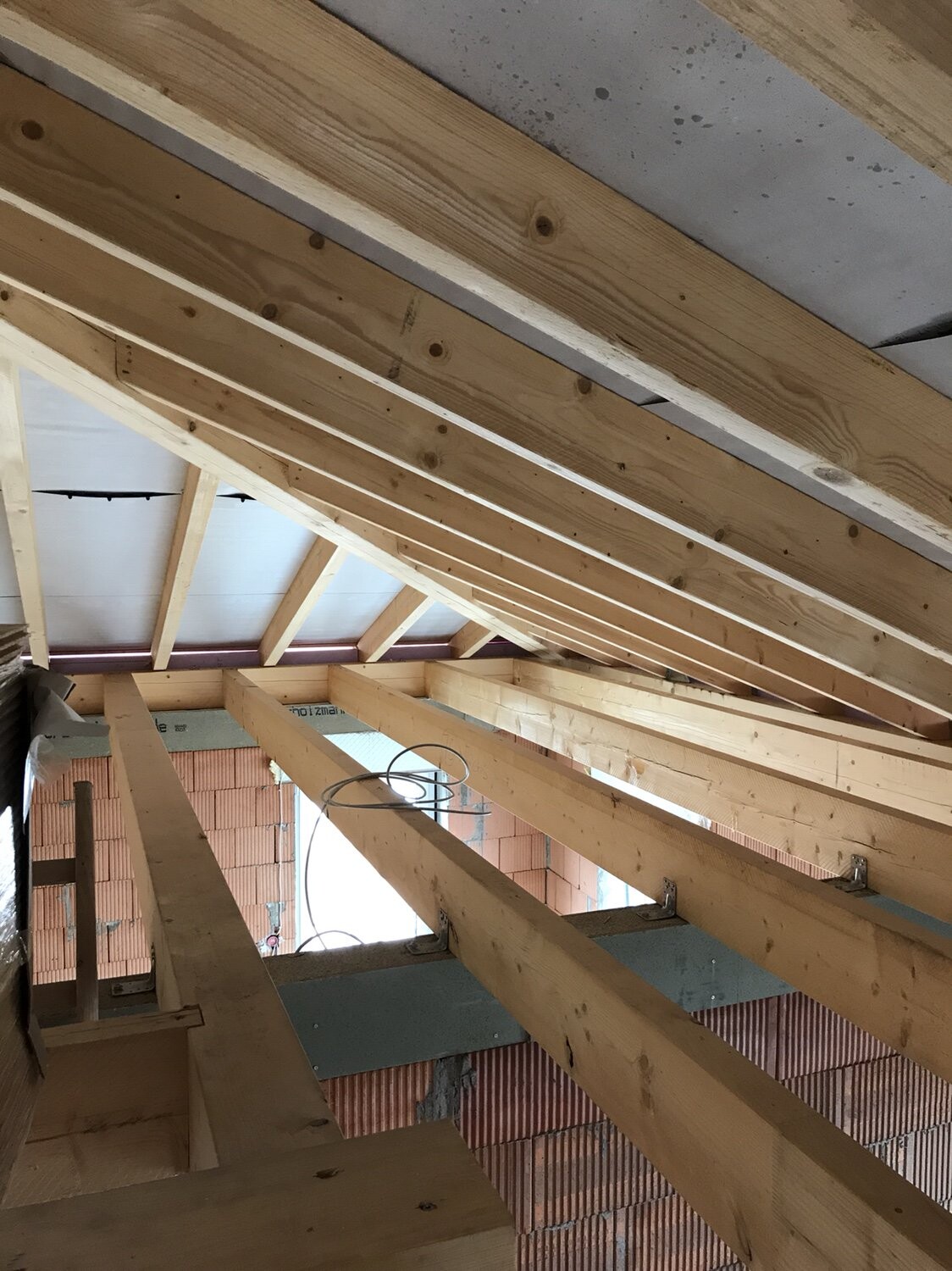 Shell construction: wooden roof frame with rafters, exposed cables, red brick walls.