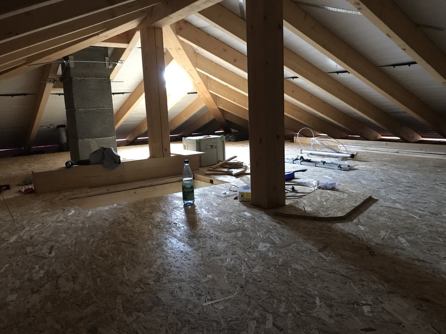 Attic under construction: wooden beams, supports, OSB floor, tools and water bottle.