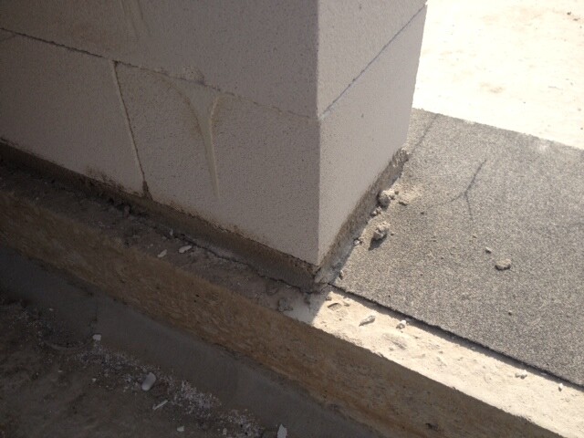 Corner area of a shell construction: concrete wall on foundation near asphalt, construction debris on the ground.