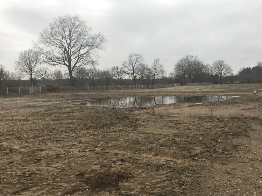 Building plot with unpaved terrain, puddles, fence and trees in the background