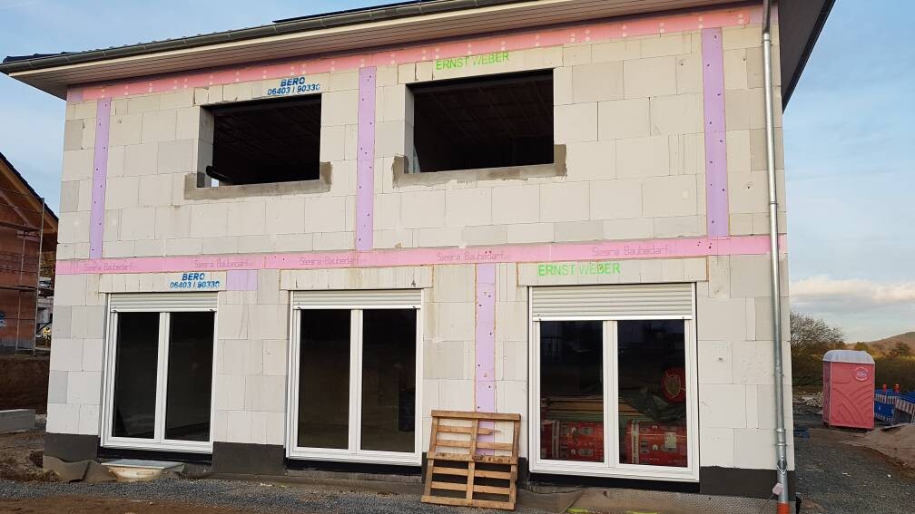 Unfertiges zweigeschossiges Haus aus Betonblöcken mit rosa Dämmstreifen und Paletten davor