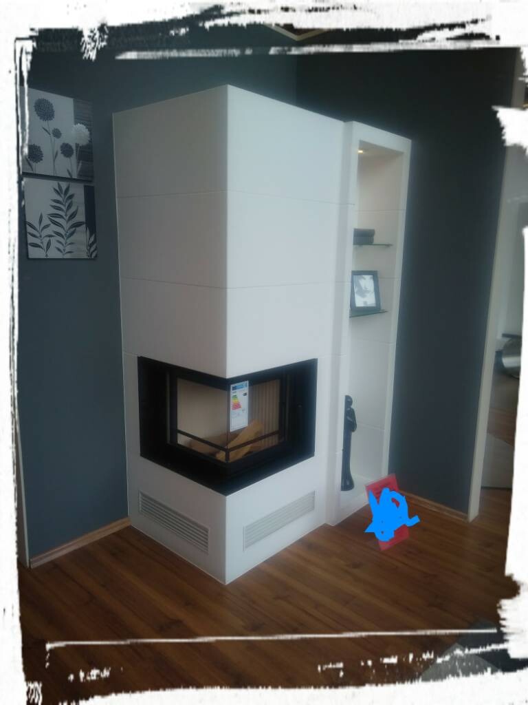 Modern white fireplace with glass front against dark blue wall, wooden floor; shelf on the right.