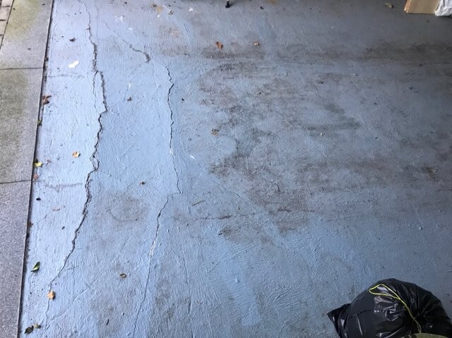 Gray concrete floor with cracks; edge of paving stones on the left, black garbage bag bottom right.